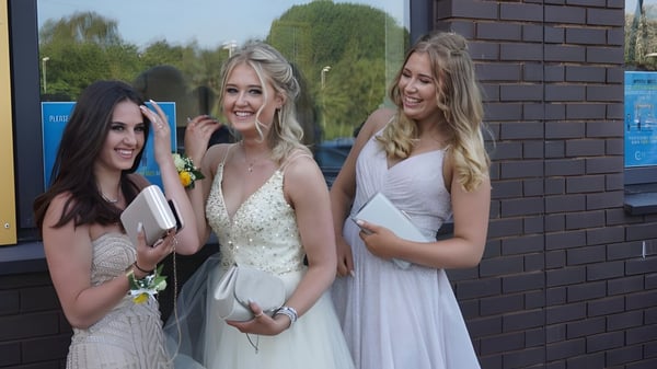 Drei Schülerinnen der Hanham Woods Academy stehen in formeller Kleidung vor einem Backsteingebäude mit Grünpflanzen.