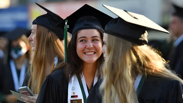 Eine lächelnde Absolventin in Talaren steht mit anderen Graduierenden auf dem Gelände der Harbour View High School.
