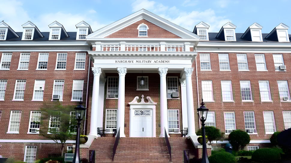 Das Backsteingebäude der Hargrave Military Academy mit einer Säulenveranda und begrüntem Vorplatz ist von einem gepflasterten Weg umgeben.