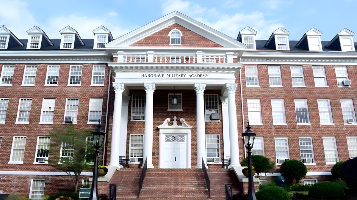 Das Backsteingebäude der Hargrave Military Academy mit einer Säulenveranda und begrüntem Vorplatz ist von einem gepflasterten Weg umgeben.