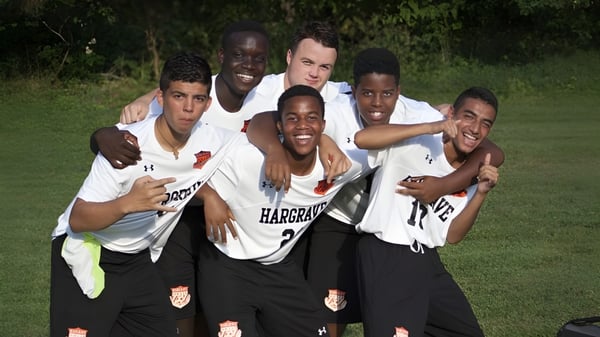 Eine Gruppe Schüler in Sportuniformen umarmt sich und lächelt auf einem Rasenfeld der Hargrave Military Academy.