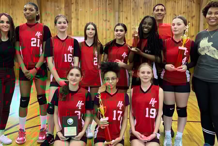 Eine Gruppe junger Athletinnen in roten Trikots posiert gemeinsam in der Turnhalle der Harmony Christian School.