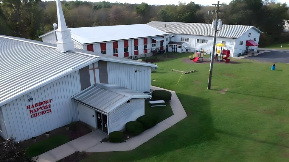 Das Gebäude der Harmony Christian School steht neben einem Spielplatz und einem grünen Bereich mit Wald im Hintergrund.