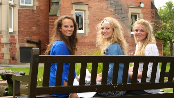 Drei Schülerinnen stehen auf einem Holzbalkon vor einem Backsteingebäude auf dem Campus des Harrogate Ladies’ College.