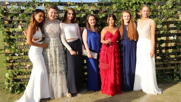 Eine Gruppe junger Frauen in festlichen Kleidern steht vor einem grünen Gartenzwischenraum am Harrogate Ladies’ College.