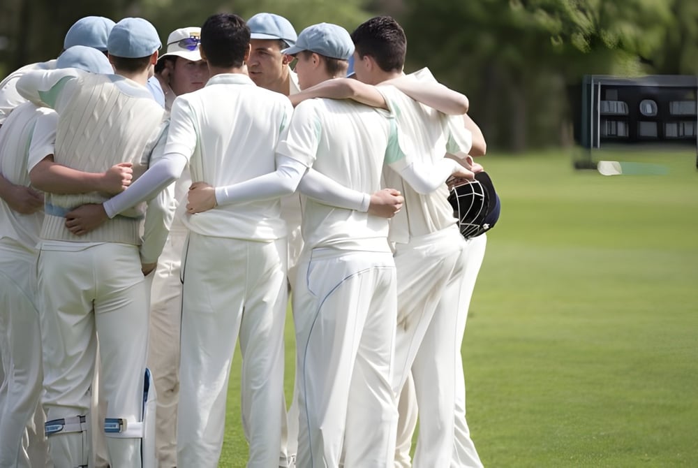 Eine Gruppe Schülerinnen und Schüler der Harrow School steht in weißen Cricket-Uniformen auf einem Rasenfeld vor einer Anzeigetafel.
