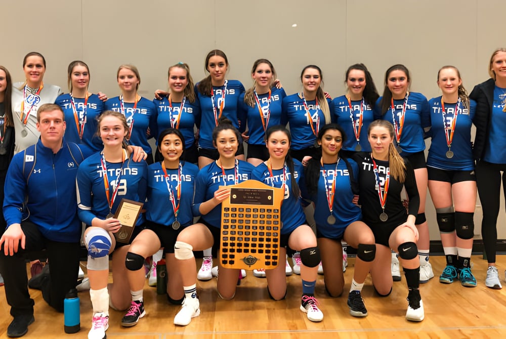 Schülerinnen der Harry Ainlay High School halten gemeinsam eine Volleyball-Trophäe auf dem Hallenboden.