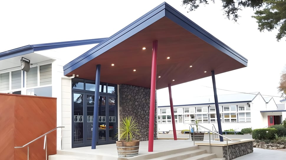 Das moderne zweistöckige Gebäude mit rotem und blauem Vordach auf dem Campus der Hastings Girls' High School ist von Bäumen umgeben.