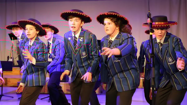 Schüler der Havelock North High School treten auf einer Bühne mit lila Hintergrund in blauen Uniformen und roten Mützen auf.