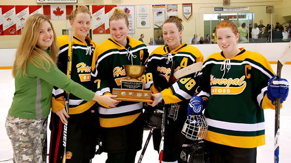 Schülerinnen des Havergal College halten eine Trophäe in einer Hockeyhalle mit kanadischen Flaggen.