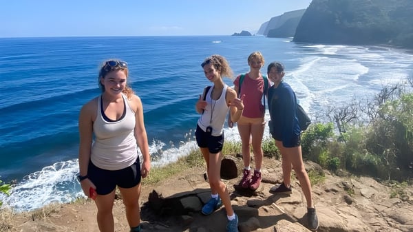 Schüler der Hawaii Preparatory Academy stehen auf einer Klippe und blicken auf den blauen Ozean und eine bergige Küste.