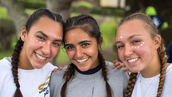 Drei Schülerinnen der Hawaii Preparatory Academy lächeln zusammen und posieren draußen vor Bäumen und Grün.