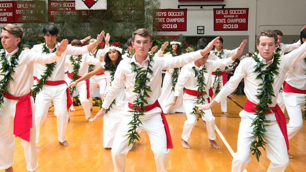 Schüler der Hawaii Preparatory Academy führen einen traditionellen Tanz mit weißen und roten Kostümen auf einer Bühne auf.