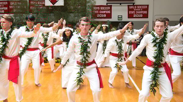 Schüler der Hawaii Preparatory Academy führen einen traditionellen Tanz mit weißen und roten Kostümen auf einer Bühne auf.