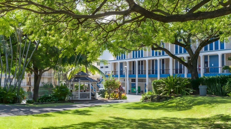 Ein grüner Garten mit Pavillon und blau-weißem Gebäude auf dem Gelände der Hawaiian Mission Academy.