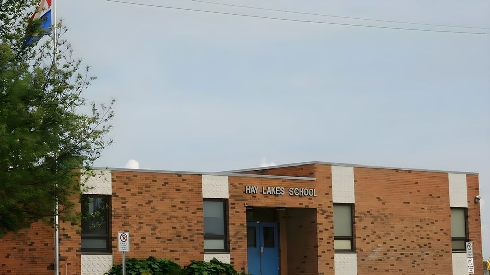 Das Backsteingebäude der Hay Lakes School ist von Bäumen umgeben und vor klarem Himmel zu sehen.
