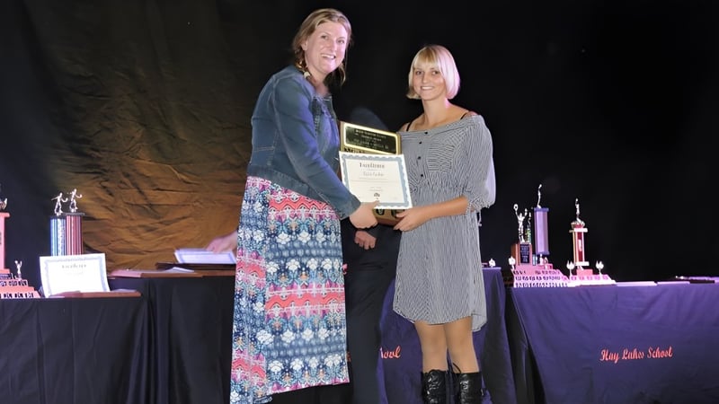 Zwei Personen stehen auf der Bühne bei der Hay Lakes School und halten gemeinsam eine Auszeichnung.