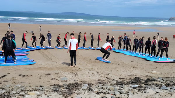 Eine Gruppe Schüler des Hazelwood College steht in Neoprenanzügen am Strand mit Surfbrettern vor dem Ozean.