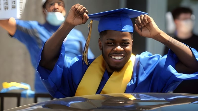 Ein junger Absolvent in blauem Abschlussgewand feiert mit erhobenen Armen auf dem Abschlussfest der H.B. Beal Secondary School.