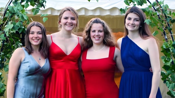 Vier junge Frauen in bunten Kleidern posieren vor einem grünen Hintergrund auf dem Campus der Headington School.