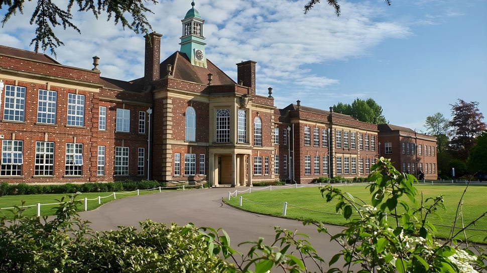 Das historische Backsteingebäude mit einem hohen Turm auf dem Campus der Headington School ist von gepflegtem Garten umgeben.