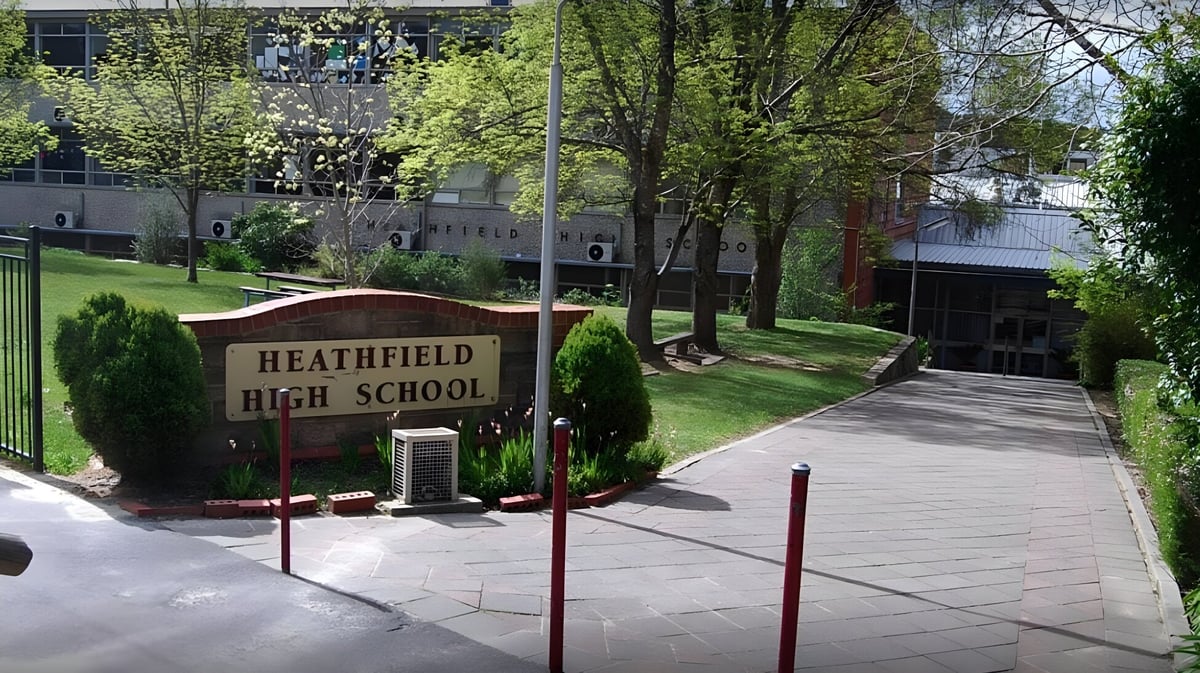 Der Eingangsbereich von Heathfield High School mit beschildertem Schulnamen und umgeben von Bäumen und Grünflächen.