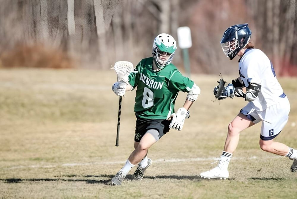 Zwei Spielerinnen in Lacrosse-Uniformen treten auf dem Spielfeld der Hebron Academy gegeneinander an.