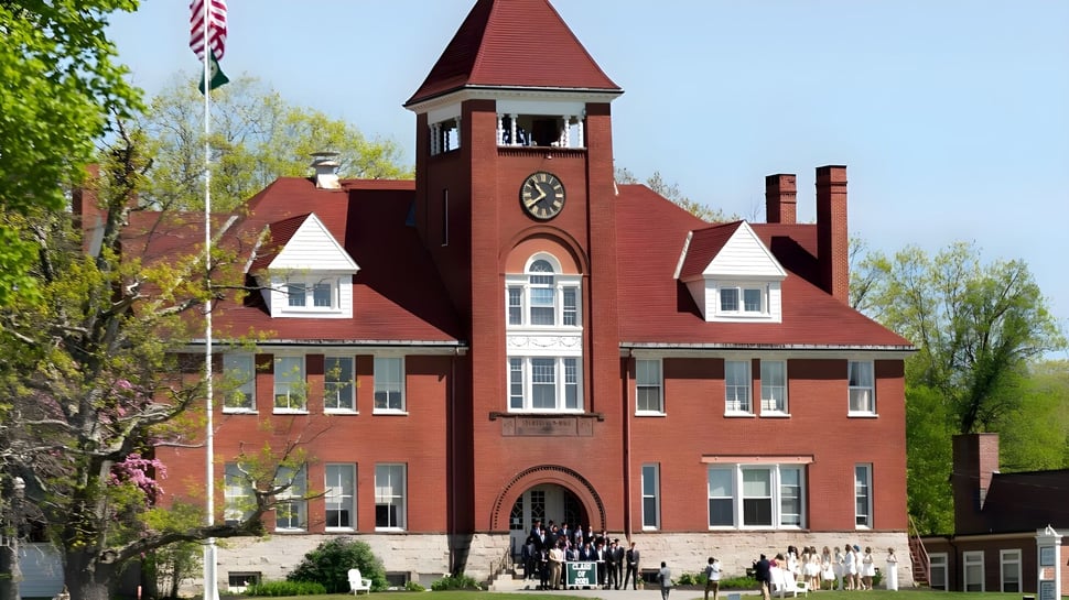 Das rote Backsteingebäude mit Uhrturm steht auf dem Campus der Hebron Academy umgeben von Grünflächen.