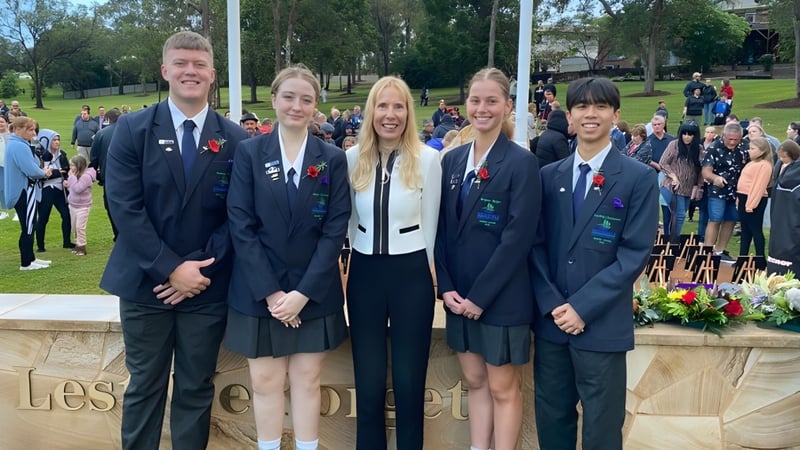 Eine Gruppe von Schülerinnen und Schülern der Helensvale State High School steht in formeller Kleidung vor einer Steinstruktur im Freien.