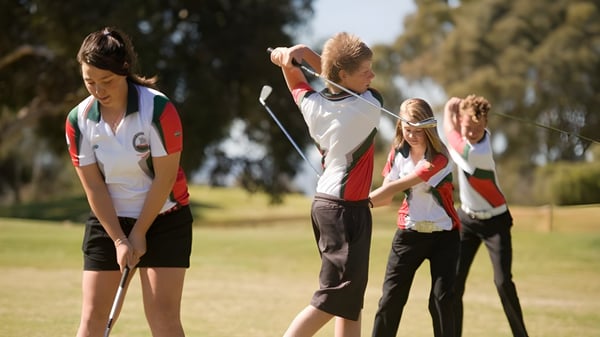 Eine Gruppe Schüler in Sportkleidung steht auf einem Sportplatz der Henley High School bei klarem Himmel.