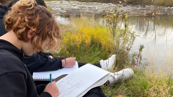 Eine Person schreibt in einem Notizbuch neben einem Teich in der Natur auf dem Gelände der Henry Wise Wood High School.
