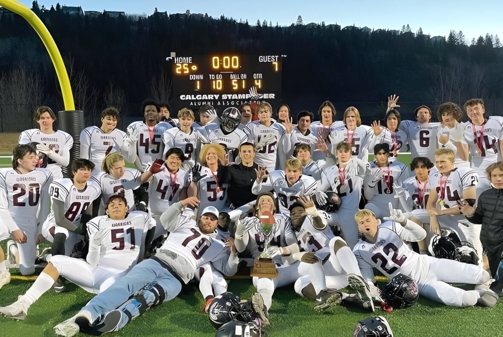 Eine Gruppe von Schülerinnen und Schülern spielt Fußball auf dem Feld der Henry Wise Wood High School mit Anzeigetafel im Hintergrund.