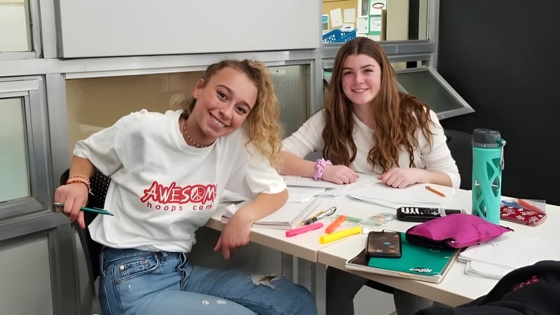 Zwei Schülerinnen der Henry Wise Wood High School sitzen an einem Tisch und lernen gemeinsam mit Schulmaterialien.