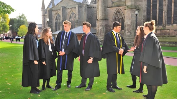 Eine Gruppe von Schülern in Abschlussroben steht vor einem großen Steinbau auf dem Campus der Hereford Cathedral School.