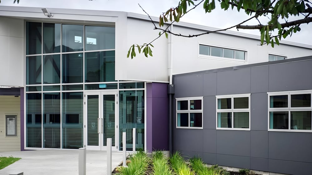 Das moderne und mehrstöckige Hauptgebäude des Heretaunga College mit Glaswänden und lila Akzenten ist von Bäumen umgeben.