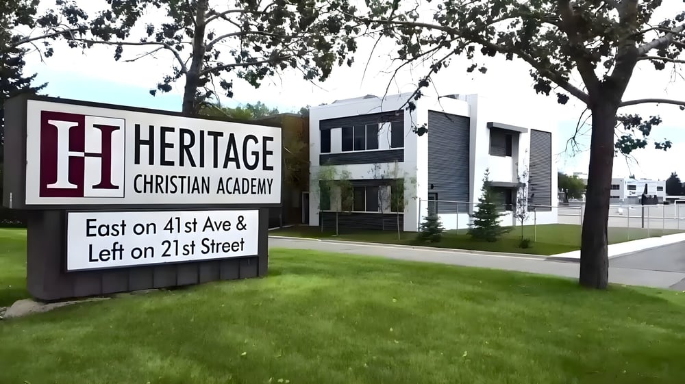 Das große Schild der Heritage Christian Academy mit Schulgebäude und Rasenfläche im Hintergrund.