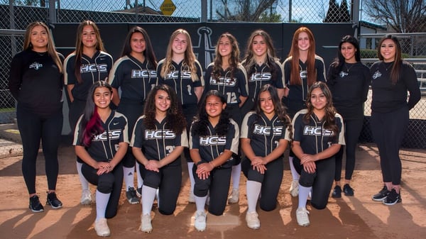 Eine Gruppe junger Sportlerinnen der Heritage Christian School posiert gemeinsam auf dem Sportplatz vor Zaun und Bäumen.