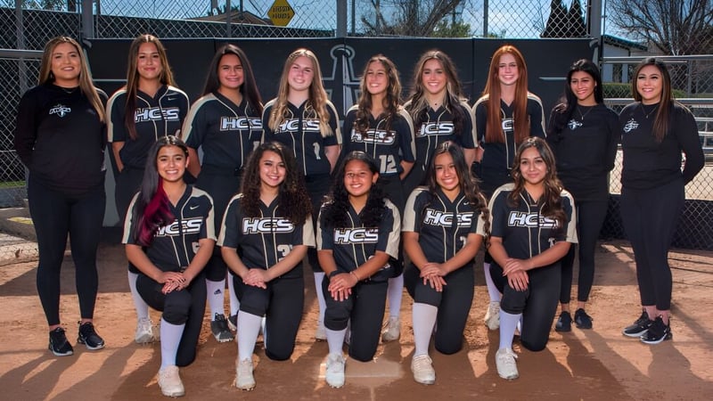 Eine Gruppe junger Sportlerinnen der Heritage Christian School posiert gemeinsam auf dem Sportplatz vor Zaun und Bäumen.