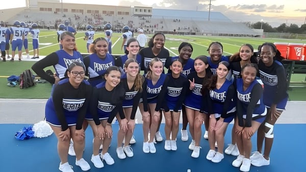 Eine Gruppe von Cheerleadern in blauen und weißen Uniformen steht auf dem Sportfeld der Heritage High School.