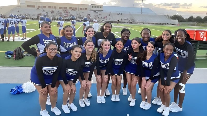 Eine Gruppe von Cheerleadern in blauen und weißen Uniformen steht auf dem Sportfeld der Heritage High School.