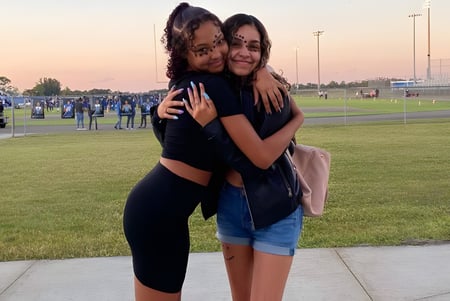 Zwei Schülerinnen umarmen sich auf einer Wiese vor dem Sportstadion der Heritage High School.