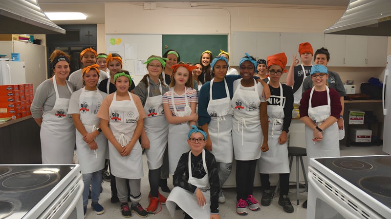 Schüler der Heritage Regional High School tragen weiße Schürzen und arbeiten in einer Schulküche mit Kochgeräten.