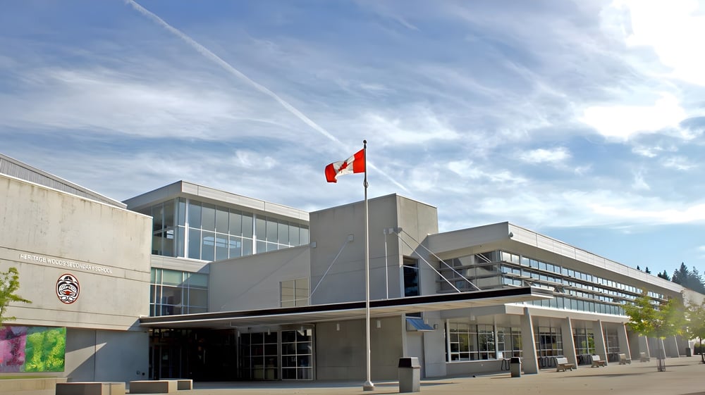 Das moderne mehrstöckige Schulgebäude der Heritage Woods Secondary School mit Glasfenstern und kanadischer Flagge im Hintergrund.