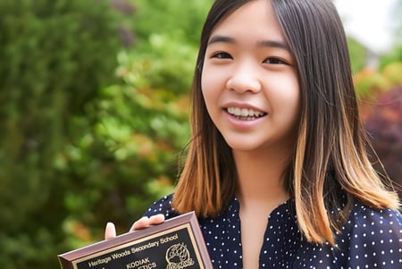 Eine Schülerin der Heritage Woods Secondary School lächelt vor grünem Laub im Hintergrund.