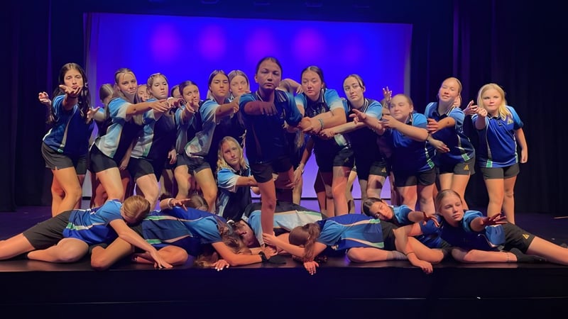 Schülerinnen der Hervey Bay State High School führen ein Tanzstück auf einer Bühne mit blauem Hintergrund auf.
