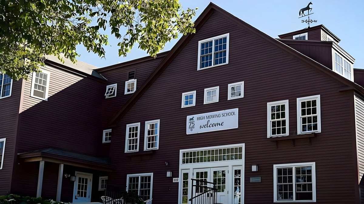Das zweistöckige Holzgebäude der High Mowing School ist von üppigem Grün und blauem Himmel umgeben.