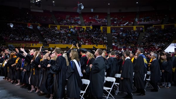 Absolventen des Higley Unified School District stehen in schwarzen Roben während der Abschlussfeier in einem vollen Auditorium.