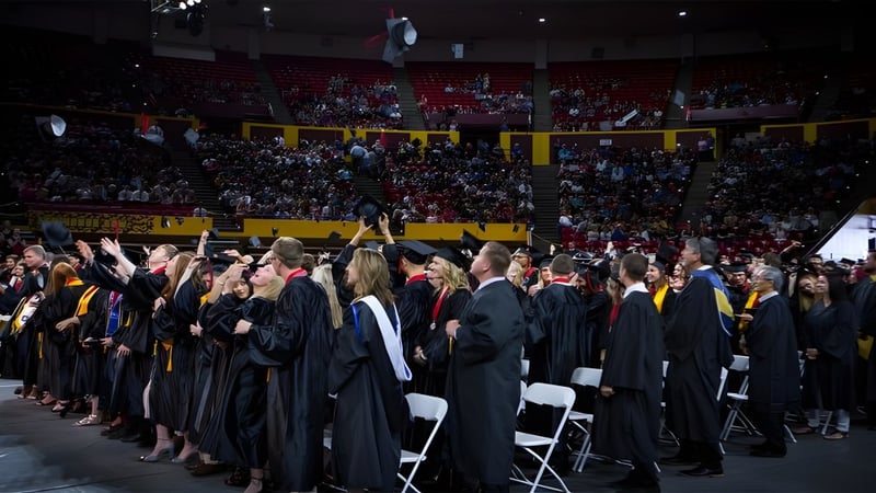 Absolventen des Higley Unified School District stehen in schwarzen Roben während der Abschlussfeier in einem vollen Auditorium.