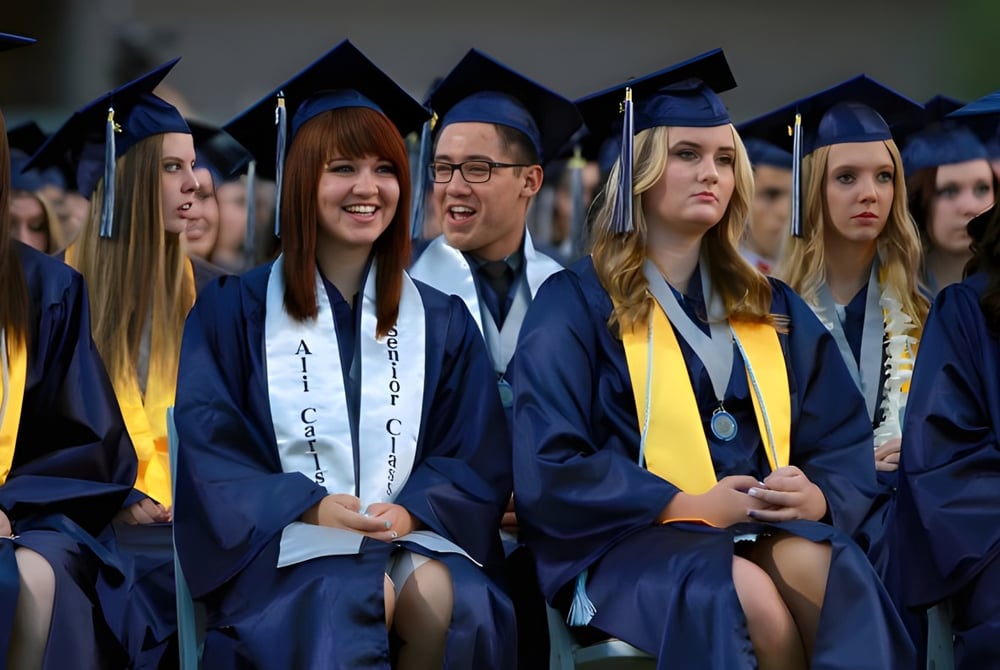 Schüler des Higley Unified School Districts tragen blaue und gelbe Abschlussgewänder und sitzen gemeinsam in einem Auditorium.