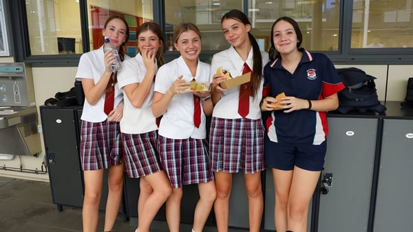 Eine Gruppe Schülerinnen im Schuluniform steht gemeinsam lächelnd im Gang des Hillcrest Christian College.